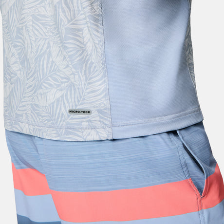 Close-up of a person wearing the Free Country Men's SunFree UPF Printed Hoodie in light blue with a subtle leaf pattern, paired with blue and coral striped shorts. The hoodie offers UPF 50+ sun protection. Right hand is tucked into the shorts pocket.