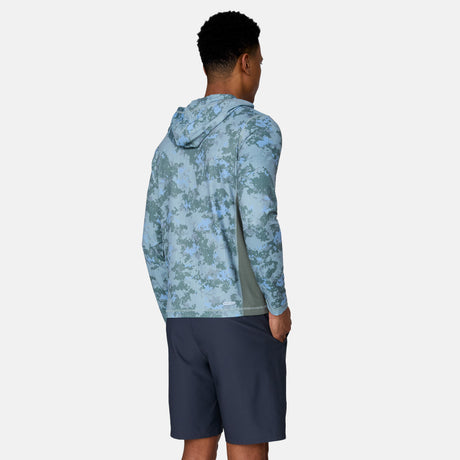 A man faces away in a Free Country Men's SunFree UPF Printed Hoodie, light blue camo pattern, hood up, paired with dark blue shorts. The recycled polyester hoodie offers UPF 50+ sun protection. Plain white background.