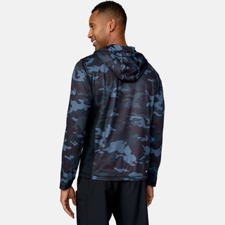 A man faces away, smiling, wearing the Free Country Men's SunFree UPF Printed Hoodie in blue and black camo with the hood up and black pants, set against a plain light gray background.