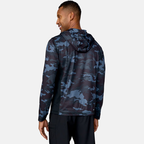 A man faces away, smiling, wearing the Free Country Men's SunFree UPF Printed Hoodie in blue and black camo with the hood up and black pants, set against a plain light gray background.