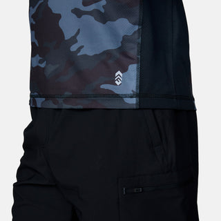 Cropped view of a person wearing black pants and the Free Country Men's SunFree UPF Printed Hoodie in blue and black camo, featuring cooling jade technology and a small white logo near the hem.