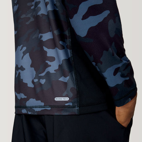 A person is shown from the back with one hand in their pocket, wearing a Free Country Men's SunFree UPF Printed Hoodie in a black and blue camo pattern with UPF 50+ sun protection, against a plain light gray background.