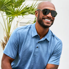 Man wearing Free Country Men's SunFree UPF Polo Shirt in Wave, size M, made from anti-odor, breathable lightweight recycled polyester performance fabric featuring a classic active fit, styled with black shorts #color_wave