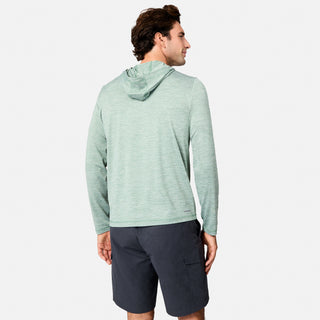 A man with short dark hair stands against a white background, wearing the Free Country Men's Textured SunFree UPF Hoodie in light green and dark gray shorts. The hoodie offers UPF 50+ sun protection and features long sleeves with a hood.
