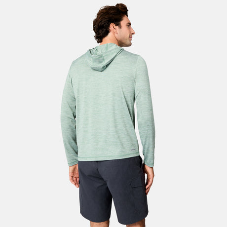 A man with short dark hair stands against a white background, wearing the Free Country Men's Textured SunFree UPF Hoodie in light green and dark gray shorts. The hoodie offers UPF 50+ sun protection and features long sleeves with a hood.