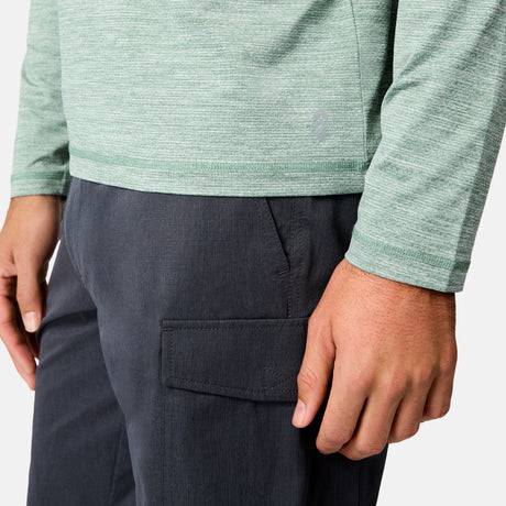 A person wearing a light green Free Country Men's Textured SunFree UPF Hoodie and dark gray cargo pants; the image shows their torso, left arm, and right hand.