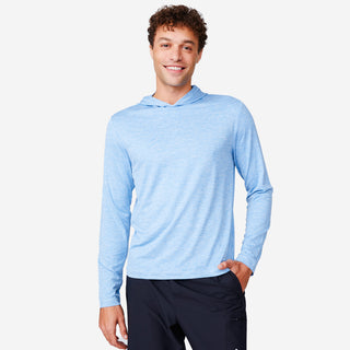 A young man with curly brown hair smiles, wearing the Free Country Men's Textured SunFree UPF Hoodie in light blue and black pants, standing with one hand in his pocket against a plain white background.