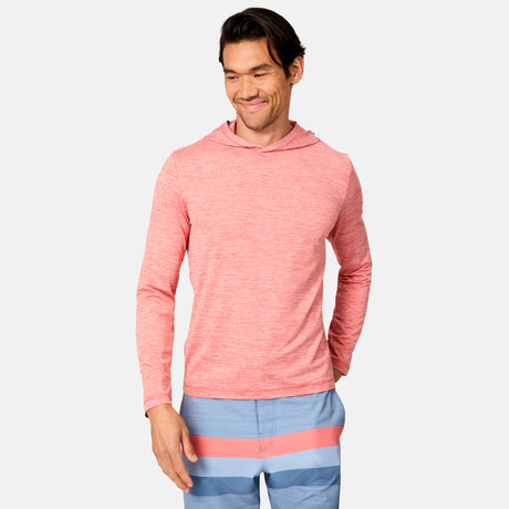 A man wearing the Free Country Men's Textured SunFree UPF Hoodie in light red and blue swim trunks with pink and coral stripes stands smiling against a plain white background.