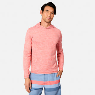 A man wears the Free Country Men's Textured SunFree UPF Hoodie in light red and blue swim trunks with pink and blue stripes, standing with one hand in his pocket against a plain light background.