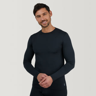 A man with short dark hair and a beard is smiling and wearing the Free Country Men's Microtech® Heat Cocarber® Coffee Base Layer Top, a fitted long-sleeve black shirt crafted from recycled materials with moisture-wicking technology, against a plain light gray background.