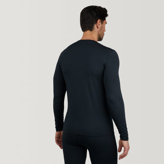 A man stands facing away, wearing a fitted, long-sleeve black Free Country Men's Microtech® Heat Cocarber® Coffee Base Layer Top, made from recycled materials with moisture-wicking properties, set against a plain light gray background.