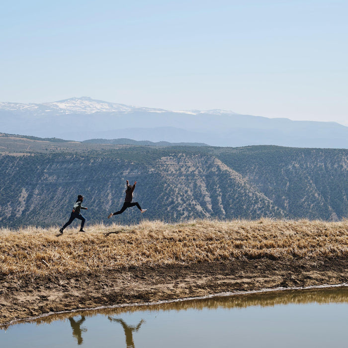Two people running on a grassy hill with mountains in the background