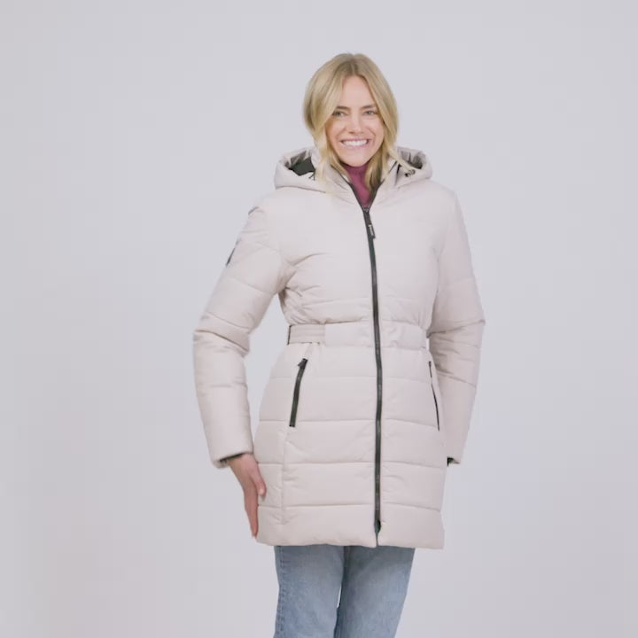 Model wearing the Women's Cirrus Quilted Long Puffer Jacket in ivory, mid-length with a hood showing off its various features like zipper pockets and adjustable waist