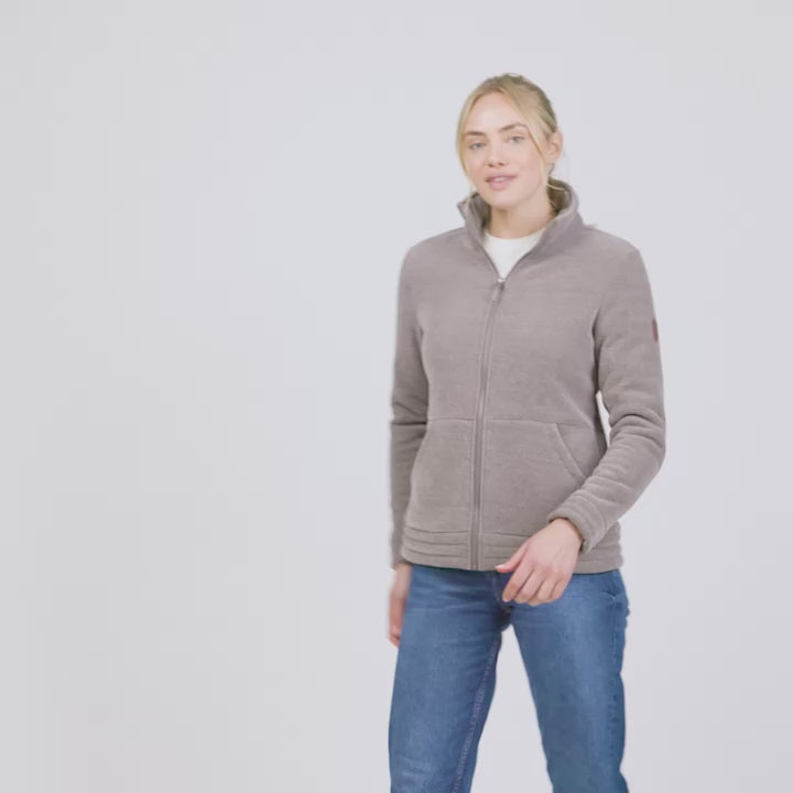 Women’s light brown zip-up fleece jacket with high collar, soft textured fabric, and dual front pockets—features a patch on the left sleeve and is styled with hands in pockets against a plain white background.