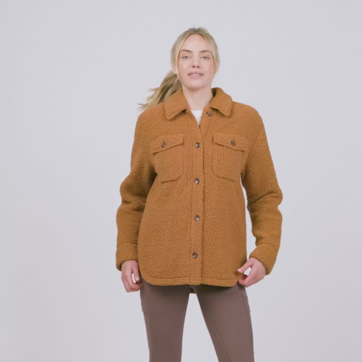 A female model wearing Free Country's women's sherpa shirt jacket, modeling its various features like pockets and button front.