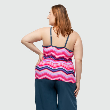 A woman with light brown hair faces away, wearing the Clearance Women's Plus Size High Neck Braided Tankini Top in pink with adjustable straps and dark blue pants, set against a plain light gray background.