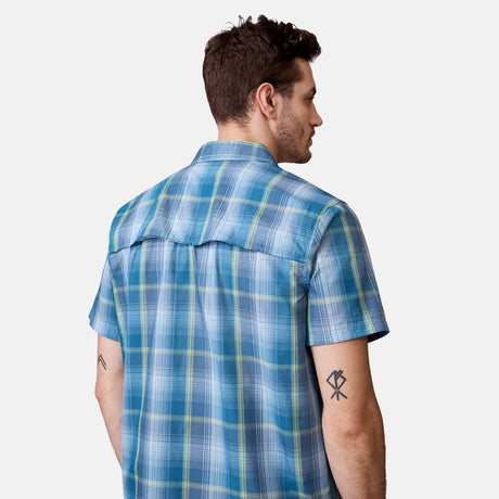 [Will is 6'2" wearing a size Medium.] Man is wearing Free Country Men's Excursion Short Sleeve Poplin Shirt in Denim Trails Plaid, size M, made from lightweight moisture wicking polyester fabric featuring vent at the back, full button down front, and a stand collar, styled with brown shorts #color_denim-trails