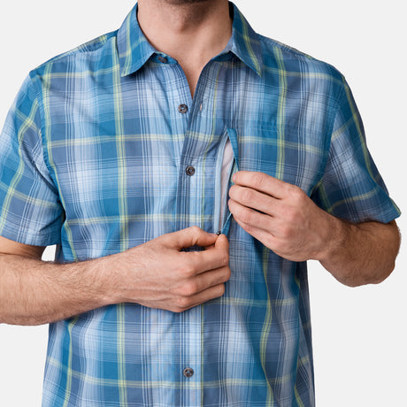 [Will is 6'2" wearing a size Medium.] Man is wearing Free Country Men's Excursion Short Sleeve Poplin Shirt in Denim Trails Plaid, size M, made from lightweight moisture wicking polyester fabric featuring vent at the back, full button down front, and a stand collar, styled with brown shorts #color_denim-trails