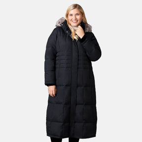 [Lola is 5'10.5" wearing a size 1X.] Woman wearing Free Country Women's Plus Size Full Length Splendor Down Jacket in black with a full front zipper opening, lower pockets, calf length, a detachable hood with faux fur trim, and water resistant and wind resistant stretch performance fabric, light grey background. Best women’s jacket for winter weather.
