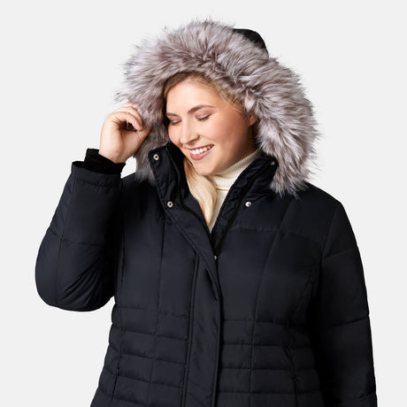 [Lola is 5'10.5" wearing a size 1X.] Woman wearing Free Country Women's Plus Size Full Length Splendor Down Jacket in black with a full front zipper opening, lower pockets, calf length, a detachable hood with faux fur trim, and water resistant and wind resistant stretch performance fabric, light grey background. Best women’s jacket for winter weather.