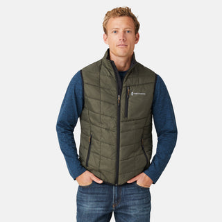 [Model is wearing a size Medium.]  Man wearing the Free Country Men's FreeCycle® Stimson Puffer Vest in green, featuring quilted design, REPREVE® poly fill, and a vertical zip, layered over a blue long-sleeve shirt with dark jeans.