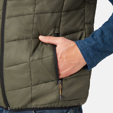 [Model is wearing a size Medium.]  Man wearing the Free Country Men's FreeCycle® Stimson Puffer Vest in green, featuring quilted design, REPREVE® poly fill, and a vertical zip, layered over a blue long-sleeve shirt with dark jeans.