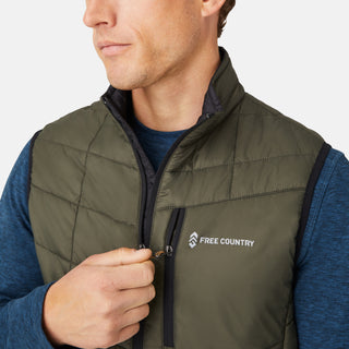 [Model is wearing a size Medium.]  Man wearing the Free Country Men's FreeCycle® Stimson Puffer Vest in green, featuring quilted design, REPREVE® poly fill, and a vertical zip, layered over a blue long-sleeve shirt with dark jeans.