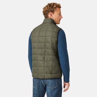 [Model is wearing a size Medium.]  Man wearing the Free Country Men's FreeCycle® Stimson Puffer Vest in green, featuring quilted design, REPREVE® poly fill, and a vertical zip, layered over a blue long-sleeve shirt with dark jeans.