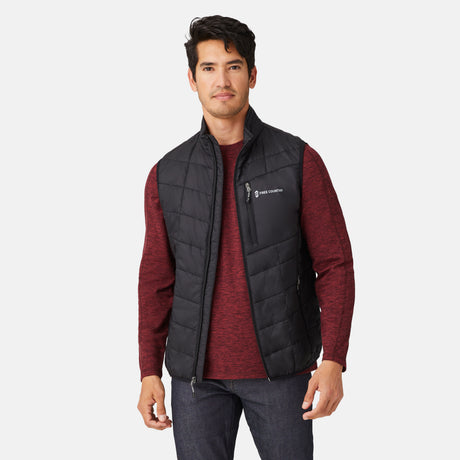 [Model is wearing a size Medium.] Man wearing the Free Country Men's FreeCycle® Stimson Puffer Vest in black, featuring quilted design, REPREVE® poly fill, and a vertical zip, layered over a burgundy long-sleeve shirt with dark jeans.