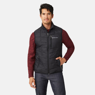 [Model is wearing a size Medium.] Man wearing the Free Country Men's FreeCycle® Stimson Puffer Vest in black, featuring quilted design, REPREVE® poly fill, and a vertical zip, layered over a burgundy long-sleeve shirt with dark jeans.