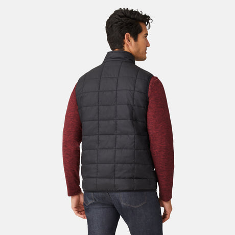 [Model is wearing a size Medium.] Man wearing the Free Country Men's FreeCycle® Stimson Puffer Vest in black, featuring quilted design, REPREVE® poly fill, and a vertical zip, layered over a burgundy long-sleeve shirt with dark jeans.