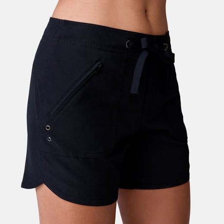 [Model is 5’9” wearing a size Small.] Woman wearing Free Country Women's 5" Bermuda Board Short in Black, size S, made from quick drying UPF stretch performance fabric featuring a fly front zipper closure with a drawcord and two front pockets 