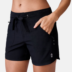 [Model is 5’9” wearing a size Small.] Woman wearing Free Country Women's 5" Bermuda Board Short in Black, size S, made from quick drying UPF stretch performance fabric featuring a fly front zipper closure with a drawcord and two front pockets 